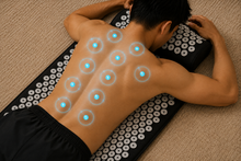 A man lies face down on a black massage/acupressure mat with rows of white circular knobs, placed on a beige carpet. Glowing blue circles highlight specific back pressure points.
