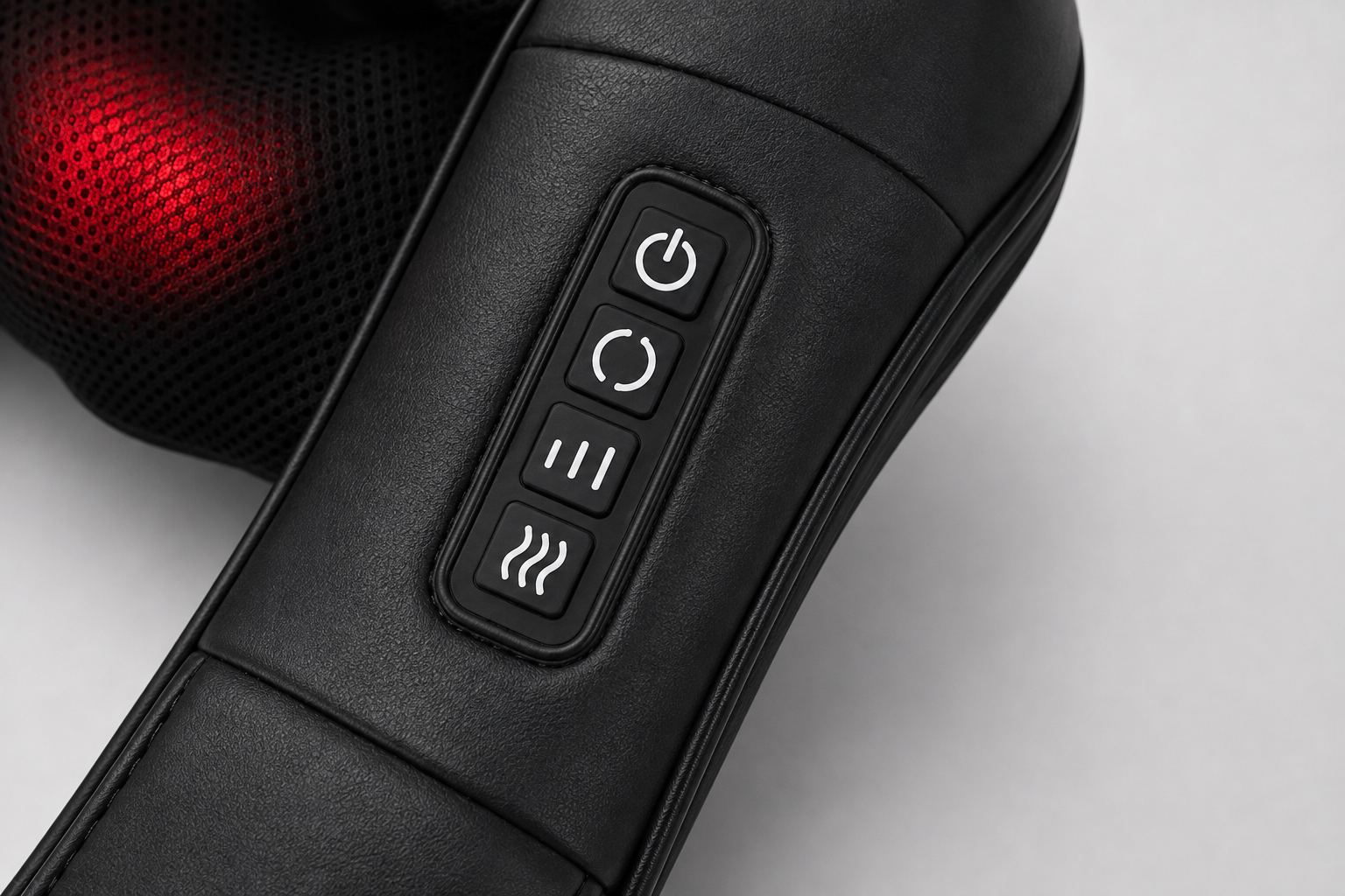 Close-up of a black massage device with a control panel showing power, mode, pause, and heat symbols, with a red illuminated mesh section in the background.