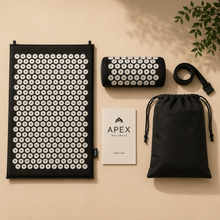 APEX Wellness massage/acupressure kit laid out on a beige surface, including a black rectangular massage board with circular pressure points, a matching cylindrical pouch, a black strap, a black drawstring bag, and a white branded card.