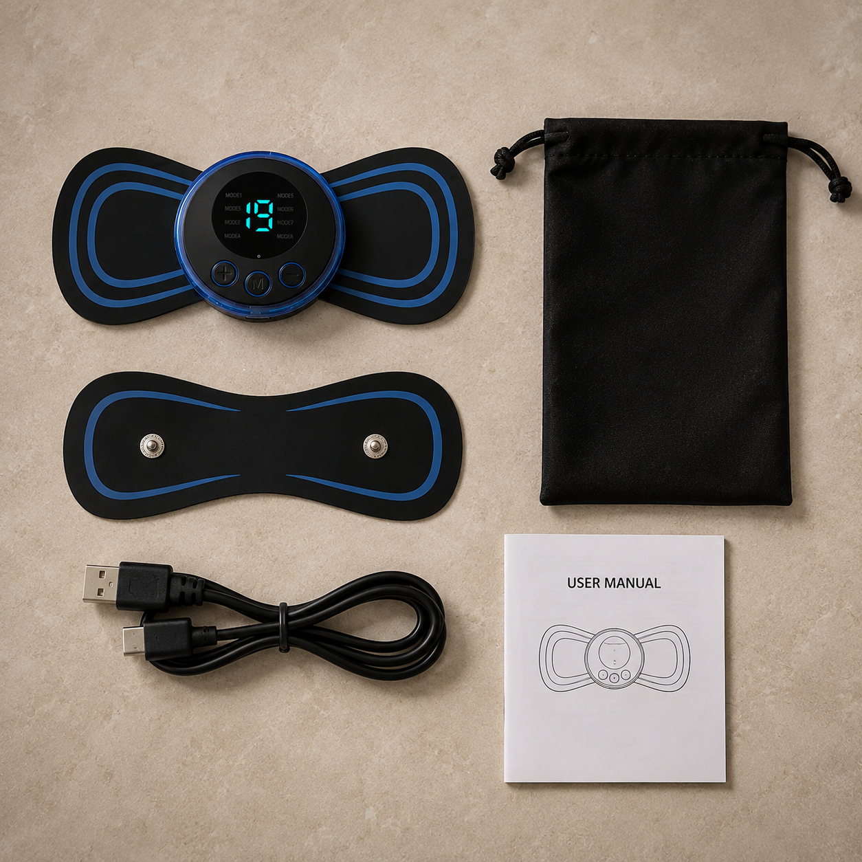 An electric muscle stimulator TENS unit kit laid out on a beige stone surface, including a black and blue controller pad, two black and blue electrode pads, a black USB charging cable, a black drawstring storage bag, and a white user manual.